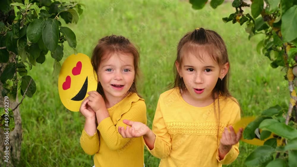 Wall mural Girls in the garden under a tree hide behind cardboard faces of happy emoticons. world smile day