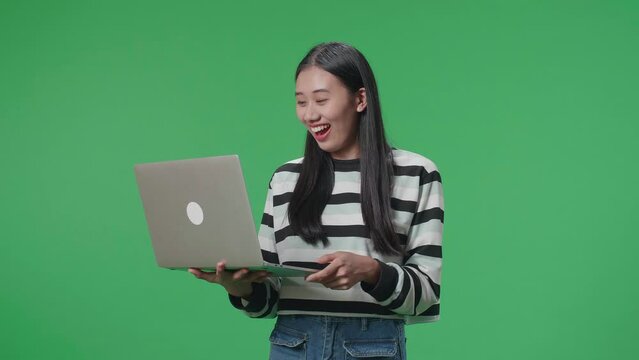 A Smiling Asian Woman Saying Wow While Using Computer On The Green Screen Background
