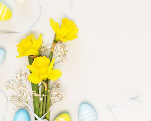 Easter holiday composition with bouquet of yellow daffodils with ribbon and easter eggs on a white background with copy space suitable for congratulation or invitation