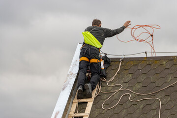 A repairman throws an electric cable from the top of the roof.