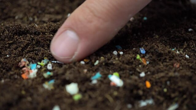 Microplastics inside the soil. Concept of global warming and climate change. Non-recyclable plastic pollution in the soil. Person examining the micro plastics with his index finger.