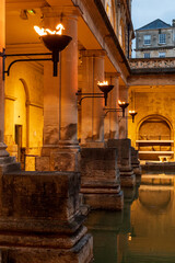 City of Bath, UK. Evening sightseeing of restored in Victorian times ancient Roman Baths in the fire light of wall sconces.