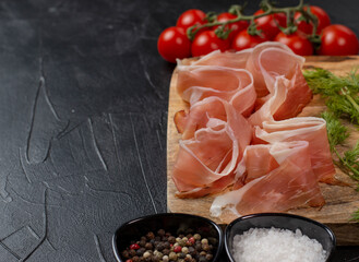 Prosciutto crudo parma ham, dry cured pork meat on a wooden board. Black background. Copy space....
