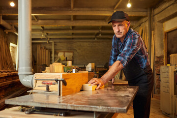 Senior carpenter in uniform works on a woodworking machine at the carpentry manufacturing