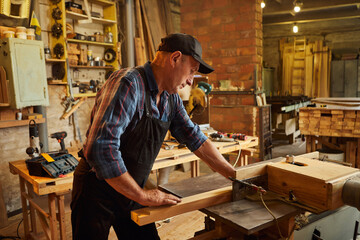 Senior carpenter in uniform works on a woodworking machine at the carpentry manufacturing