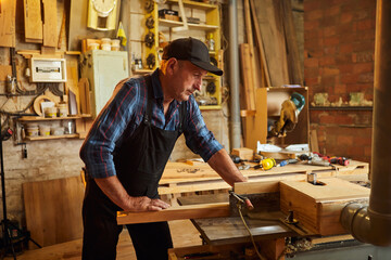 Senior carpenter in uniform works on a woodworking machine at the carpentry manufacturing