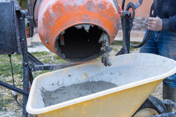 Man busy doing masonry work, mixing concrete with an electric cement mixer, wheelbarrow and shovel....