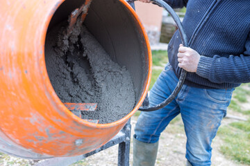 Man busy doing masonry work, mixing concrete with an electric cement mixer, wheelbarrow and shovel. bonus 110%, superbonus.