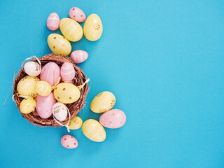 Flat lay composition of yellow and pink easter eggs in basket blue background with space for text.