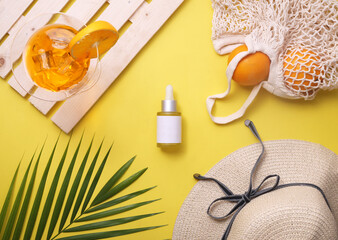 Flat lay of Vitamin c skin care products. Summer props like hat, oranges, palm leaf, goggles in the background. Top view.