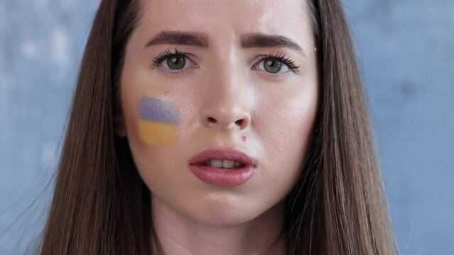 Outdoor portrait of young girl with blue and yellow ukrainian flag on her cheek. Stop war in Ukraine. Russia stop war.