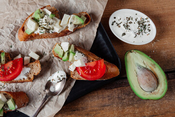 Sandwiches with pasta,avocado, tomato. Whole grain bread. Vegan sandwich from vegetables on black cutting board. Wooden background