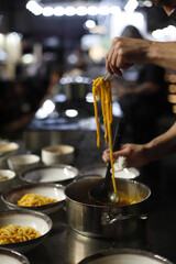 Chef trabajando en cocina un plato de pasta con salsa elevándola con un tenedor en sus manos