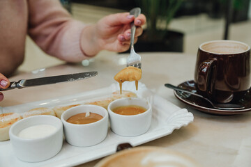 Lovely women enjoys breakfast in a cafe. Breakfast food. Coffee, cheesecakes, sauce on the table