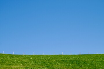 Summer landscape - field with green grass and wooden fence against blue sky.