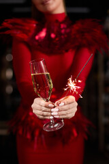 A girl in an elegant dress holds a glass of champagne and sparklers in her hands