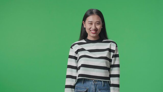 A Smiling Asian Woman Dabbing While Standing In Front Of Green Screen Background  
