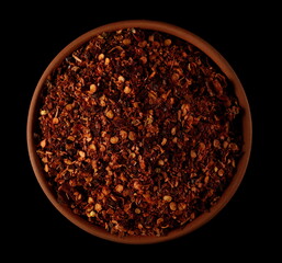 Spicy chili pepper flakes, crushed, milled dry red  pile in clay pot isolated on black, top view