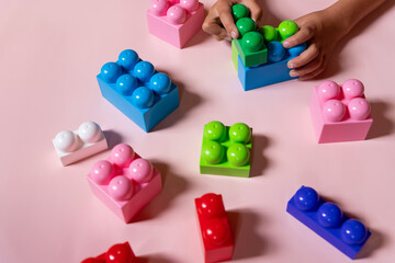 Top view on child's hands playing with colorful plastic bricks on pink table .Kid building with geometric shapes. Learning and education concept.Building blocks background. Developing toys, game