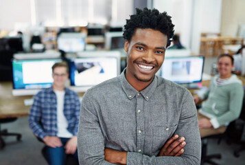 We turn ideas into reality. Portrait of a young man standing in an office with designers in the background.