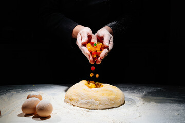 women's hands knead dough with candied fruits for easter cakes. black background