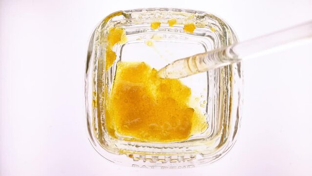 Marijuana concentrate wax in a small glass container.  Flat lay top view of live sugar wax, person using a glass dabber to get a dose of wax for use.  Macro view of drug preparation.