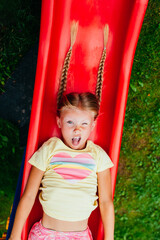 Fototapeta na wymiar Funny little girl playing on a slide at a playground. Childhood. Happy kid