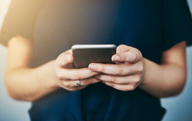 Downloading a new app. Studio shot of an unrecognizable young woman using her cellphone against a grey background.