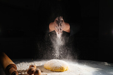 women kneads dough and scatters flour on a black background.