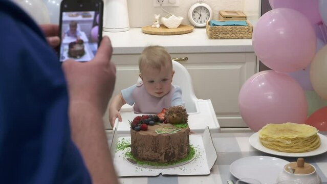 One year old baby boy celebrating his first birthday, father taking photos on mobile phone of child with sweet birthday cake. High quality 4k footage
