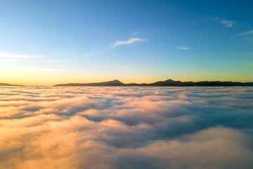 Aerial view of yellow sunset over white puffy clouds with distant mountains on horizon
