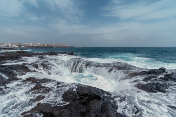 Waves beating in two holes formed in the rocks . Impressive rock formation in Telde. Gran Canaria