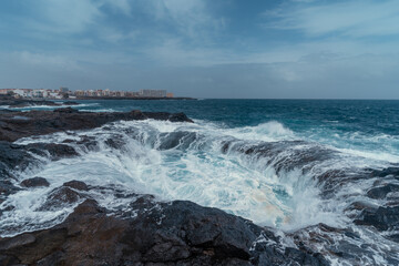 Waves beating in two holes formed in the rocks . Impressive rock formation in Telde. Gran Canaria