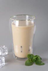 Glass of traditional Indian lassi drink with mango and ice on a grey background. Vertical orientation.