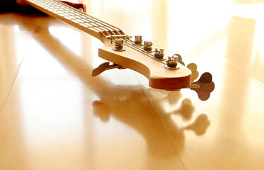 Close up of electric bass guitar with five strings. Detailed view of headstock with turning pegs of musical instrument with reflection on wooden floor. Music classes, concert, hobby and bass player co
