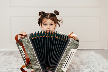 Little kid playing the accordion. Toddler girl learns how to play 
musical instrument harmonic