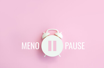Word Menopause, pause sign on a white alarm clock on pink background. Minimal concept hormone...