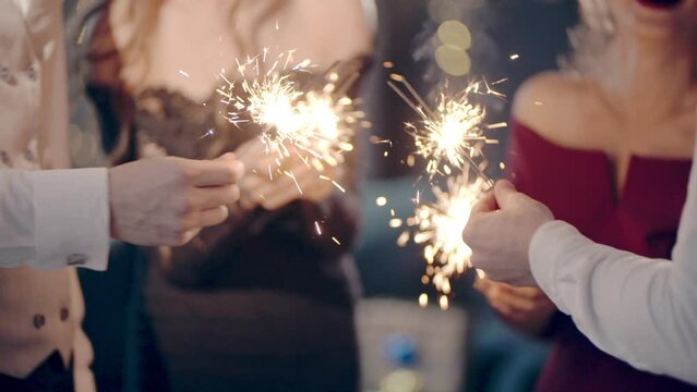 Asian girl and group young college student friends lit light sparkler in hand fireworks, sing and dance together. Woman on Party with people, love friendship relationship and celebration concept.