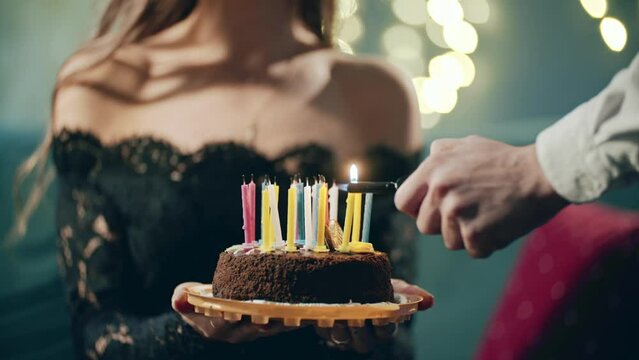Festive sweet cake with candle which lighting on lighter, burner or fire. Close up of hands holding cake on plate. Surprise for birthday, Party from friends.