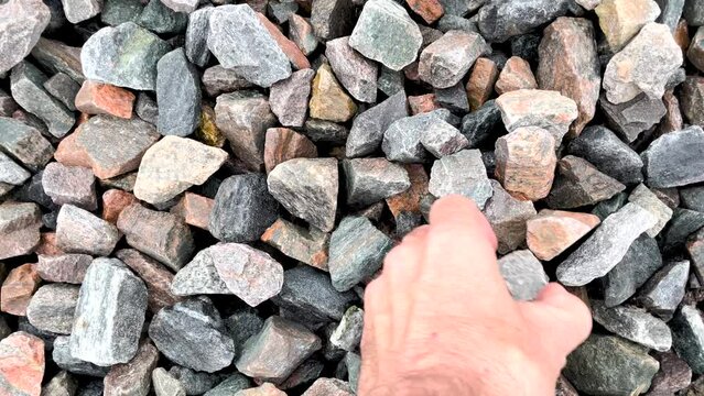 A hand picking up large rocks from a pile of rocks