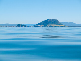 Landmark Mount Maunganui and background hills across calm idyllic blue sea