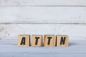 ATTN concept written on wooden cubes or blocks, on white wooden background.
