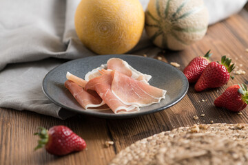 Slices of prosciutto di parma or jamon serrano (iberico) on gray plate on rustic wooden table.