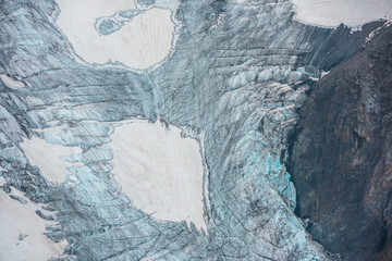 Beautiful mountain landscape with vertical glacier tongue with cracks among rocks. Awesome natural backdrop of large glacier with icefall. Nature texture of mountain glacier with fissures close up.