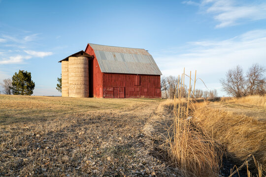 old red barn with twin silo and irrigation ditch at Colorado foothills, winter or early spring scenery at sunset
