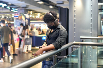 African man listening to music with the mobile while waiting in a shopping mall