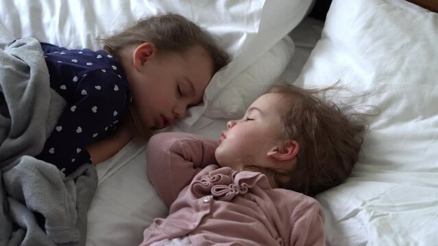 Authentic Two Cute Little Girls Sister Sleeping Sweetly Together In Comfortable White Bed. Beautiful Tired Child Have Rest Time Gently Soothing. Kids Resting. Care, Childhood, Parenthood, Life concept