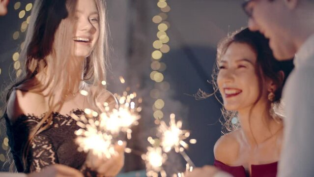 Asian girl and group young college student friends lit light sparkler in hand fireworks, sing and dance together. Woman on Party with people, love friendship relationship and celebration concept.