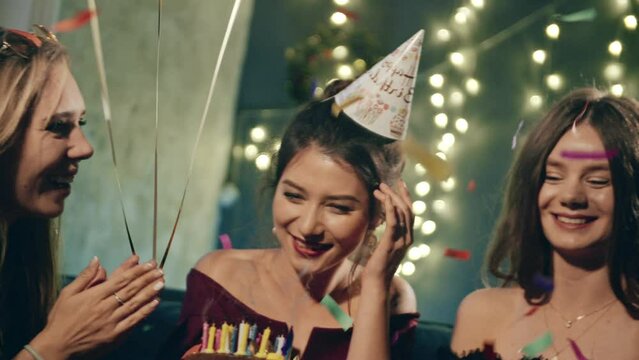 Young woman blowing out fire on candles and making wish at party or celebration. Close-up portrait of smiling asian girl and friends making surprise and taking out birthday cake with candles.