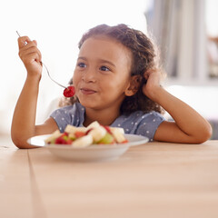 Who knew it would be so yummy. Shot of a cute little girl eating fruit salad at a table.